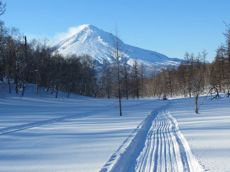 Snowmobile along a snowy trail. Mountain and trees in background.