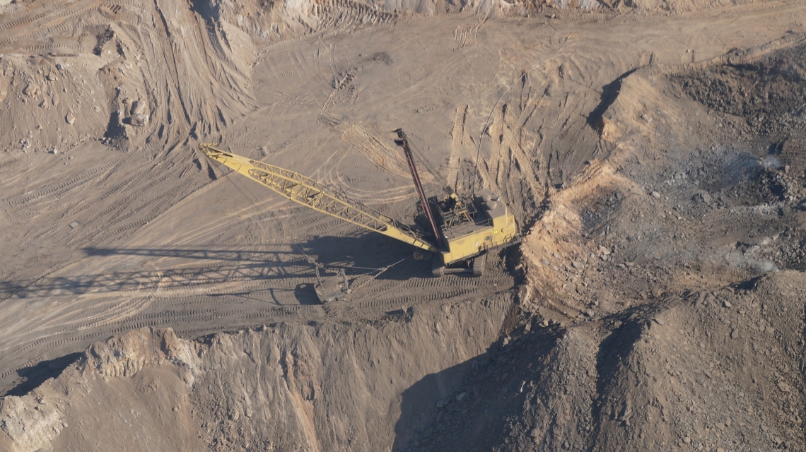 aerial view of open pit mine, with an excavator pictured in the middle