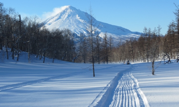 Snowmobile along a snowy trail. Mountain and trees in background.